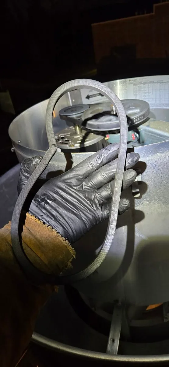 Technician holding drive belt during exhaust fan belt replacement on rooftop unit in South Jersey
