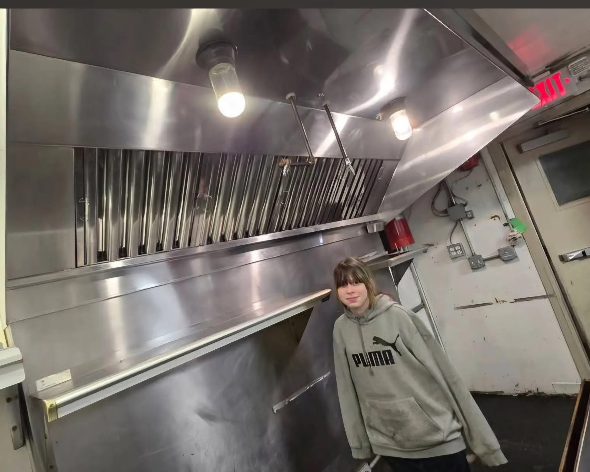 Tyler's daughter posing next to a clean commercial hood in a South Jersey food truck kitchen